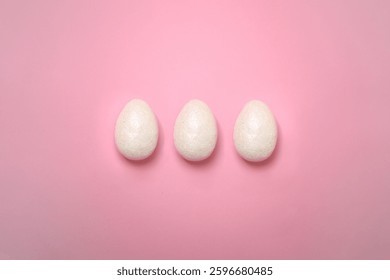A simple and elegant composition of three white Easter eggs placed in the center of a pastel pink background. Ideal for holiday-themed designs, greeting cards, and creative projects. sstkEaster