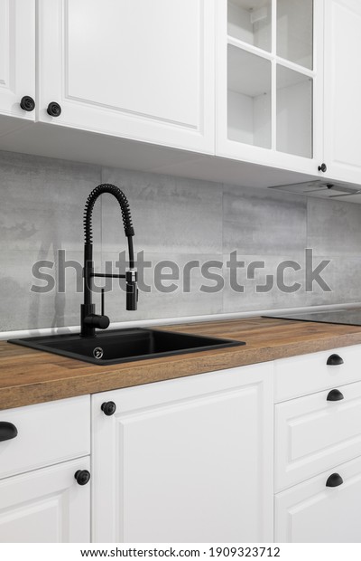 Simple and elegant kitchen with\
wooden countertop, white cupboards, drawers and black\
sink