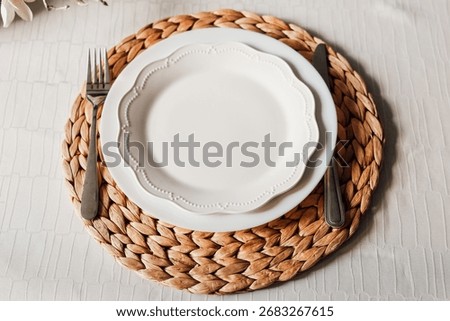 A simple and elegant table setting features a white plate placed on a woven charger. Fork and knife are neatly arranged beside the plate creating a welcoming atmosphere for a meal.