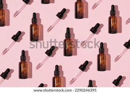 Simple face skincare pattern made with dark brown glass serum or essential oil bottle and dropper on pastel pink background. Minimal fresh product aesthetic.