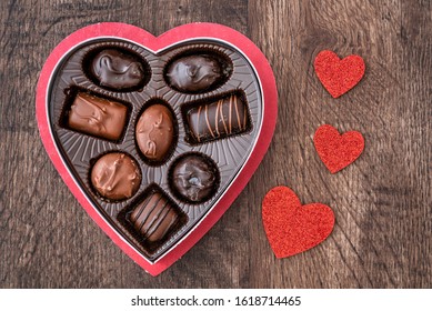 Simple heart shaped box of chocolate Valentine’s Day candy on a wood table, with red glitter hearts
 - Powered by Shutterstock