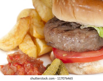 Simple home made basic hamburger with tomato slices, lettuce and onion in a white bread bun with chips and pickles.