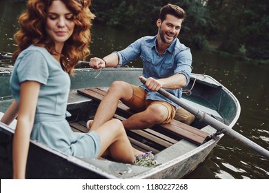 Simple joy of loving. Beautiful young couple enjoying romantic date and smiling while rowing a boat