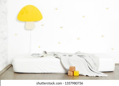 Simple kid's bedroom interior with a white mattress on the floor and yellow mushroom lamp on the wall
