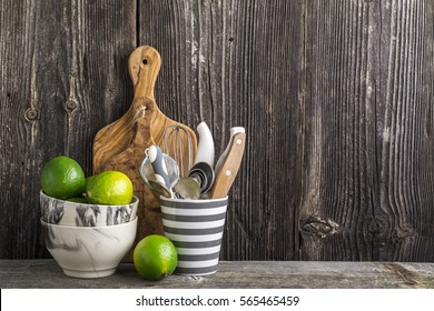 Simple kitchen still life on a background of a wooden wall on a shelf with cutlery, tools, marble bowls and juicy limes. The concept of home comfort food and comfort.