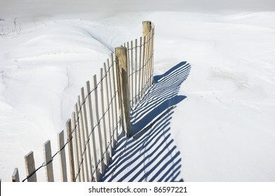Simple landscape of sand fence and shadows on snowy white dunes at the beach. Sand fences play a vital part in conserving and growing sand dunes. Tiny bird tracks are evident to the left of the fence.