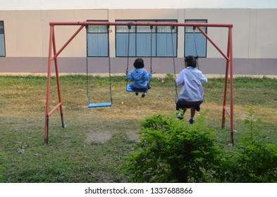 Simple life without technology - two school girls wearing school uiform, white shirt and blue skirt, are riding on a swing in a playground before afternoon classes begins with happiness