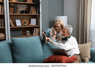 Simple living. Happy middle-aged senior couple 70s husband and wife sit relax on couch in living room reading book drinking tea together, calm elderly 60s couple booklovers rest at home enjoy life - Powered by Shutterstock