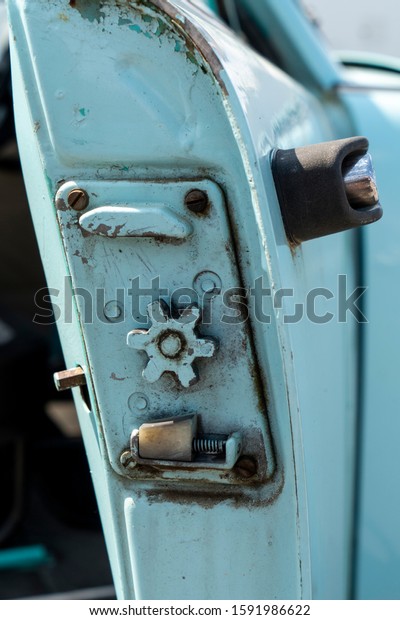 Simple mechanical car door lock on an old\
utilitarian duck egg blue Russian car. Six large spokes on a metal\
cog wheel and a spring engage the locking mechanism.  Four rusty\
screws hold the plate.