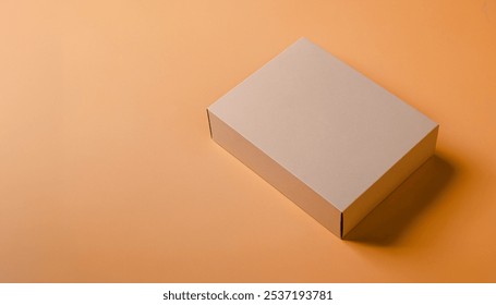 Simple, minimalist shot of a tan cardboard box on an orange background. Premium packaging box mockup for displaying a marketing advertisement for a product.