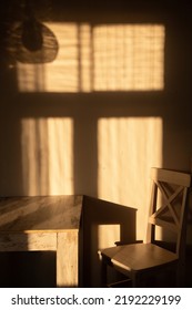 Simple Monochrome Living Room Or Kitchen Interior With Aged Wooden Table And White Chair With Shadow On The Grunge Wall From Window Frame And Late Evening Sun In Warm Yellow Colour. No People Inside