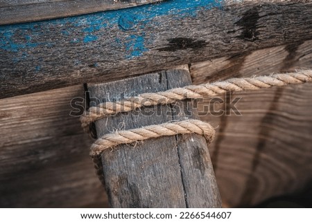 Simple natural rope tied around wooden part of fishing boat, closeup detail