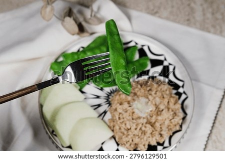 simple and nutricious breakfast featuring creamy oatmeal topped with a piece of butter, served with fresh green peas and kohlrabi on a modern white and black plate. Minimalist food styling with clean background, emphasizing healthy eating, wholesome ingredients and balanced nutrition. Ideal for healthy lifestyle, diet, wellness and breakfast concept imagery