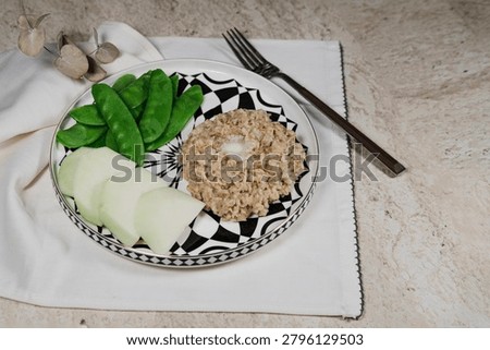 simple and nutricious breakfast featuring creamy oatmeal topped with a piece of butter, served with fresh green peas and kohlrabi on a modern white and black plate. Minimalist food styling with clean background, emphasizing healthy eating, wholesome ingredients and balanced nutrition. Ideal for healthy lifestyle, diet, wellness and breakfast concept imagery