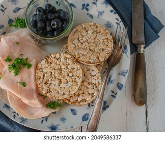 Simple Ordinary And Healthy Breakfast With Thin Sliced Chicken Breast Served With Brown Rice Cakes And Fresh Blueberries On A Plate