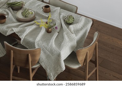 Simple organisation of dining table with ceramic dinnerware, linen tablecloth, dining chairs, artichoke and asparagus. Home decoration concept