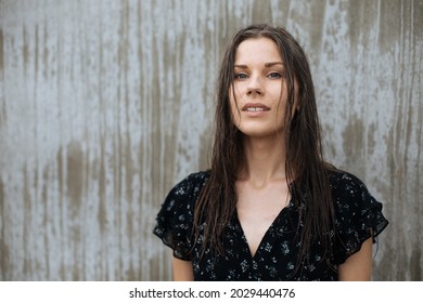 Simple portrait of a woman model next to the blank grey wall. Candid portraits of authentic people. Real life. Authentic people wearing black dress. Natural light portrait outdoors