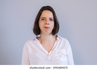 Simple Portrait Of Young Brunette Woman In White Shirt On Gray Wall Background. Business Portrait Of Employee, Manager, Casual Business Dress. Photo Of Employee. Serious Woman Without Emotion