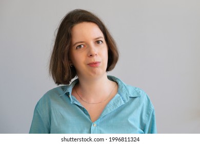 Simple Portrait Of Young Brunette Woman In Blue Shirt On Gray Wall Background. Business Portrait Of Employee, Manager, Casual Business Dress. Photo Of Employee. Serious Woman Without Emotion