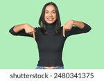 Simple portrait of a young Latina points down with fingers, positive feeling.