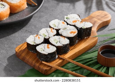 Simple roll yin yang maki on wood on gray stone background. Maki sushi with salmon and cucumber with chopsticks. Aesthetic composition with Yin yang maki sushi on concrete table. Asian food concept.