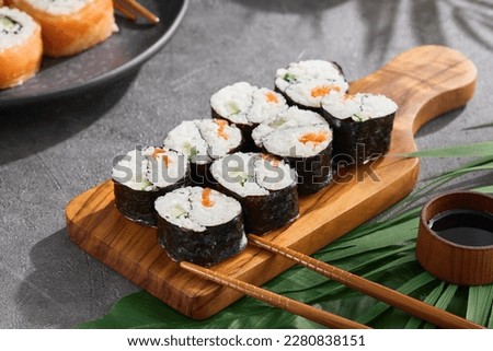 Simple roll yin yang maki on wood on gray stone background. Maki sushi with salmon and cucumber with chopsticks. Aesthetic composition with Yin yang maki sushi on concrete table. Asian food concept.