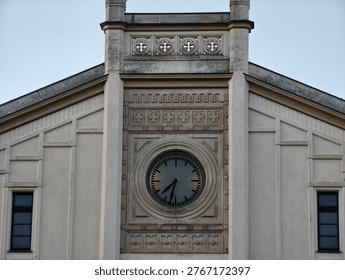 Simple round clock set in facade, clean circular face and hands against muted stone, symmetrical windows