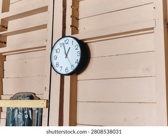 Simple round wall clock mounted on a traditional wooden wall inside a rural house. Warm natural lighting creates a cozy interior atmosphere.