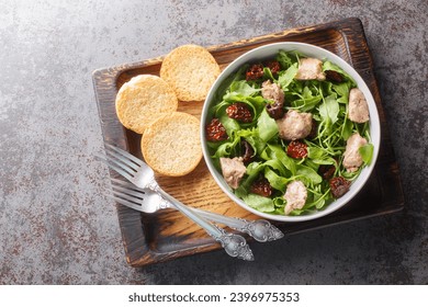Simple salad of cod liver, fresh arugula and sun-dried tomatoes served with toast close-up in a bowl on the table. Horizontal top view from above
