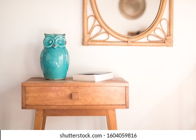 Simple side table timber with green ceramic owl figure and cane mirror on the wall 
