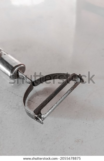 A simple stainless\
hand tool for peeling carrots and fruits.  Tool for peeling fruit\
on a white table