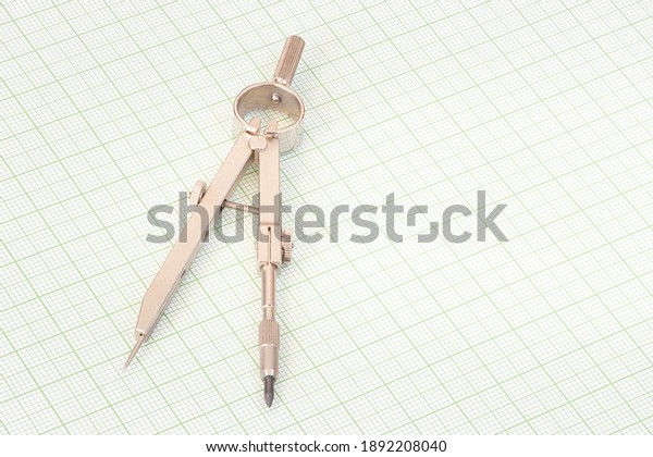 Simple steel compasses on a\
millimetre paper used for technical drawing and school\
geometry