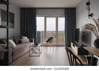 Simple and stylish living room with cozy couch, modern furniture, tv and window doors to balcony