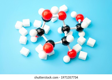 Simple Sugars, Diabetes Awareness And Chemical Structure Of Carbohydrates Concept With Plastic Model Of The Glucose Molecule And Sugar Cubes Isolated On Blue Background