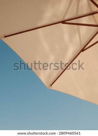 Simple summer composition of a sun umbrella corner against a blue sky in Ibiza, with warm sunlight, soft shadows, and analog film grain.