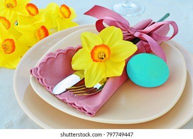 Simple table setting arrangement with cream porcelain dishes, pastel blue Easter egg, yellow daffodil flower, cutlery and napkin