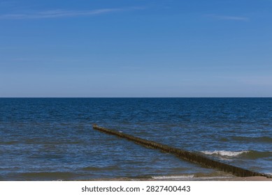 A simple timber wave breaker extends into the deep blue water, creating a clean minimalist coastal horizon in Germany. This tranquil seascape conveys serenity, environmental stability, coastal protection, and spatial freedom.