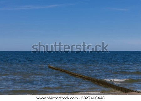 A simple timber wave breaker extends into the deep blue water, creating a clean minimalist coastal horizon in Germany. This tranquil seascape conveys serenity, environmental stability, coastal protection, and spatial freedom.