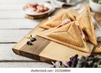 Simple triangle sandwiches filled with prosciutto slices on wooden board, homemade food on the go