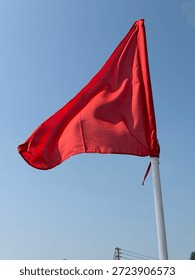A simple, triangular red flag waving against a clear blue sky.
