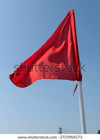 A simple, triangular red flag waving against a clear blue sky.
