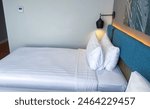 Simple twin bedroom at hotel, with neat white linen, pillow and comforter with blue headrest, double bed with stripes blanket