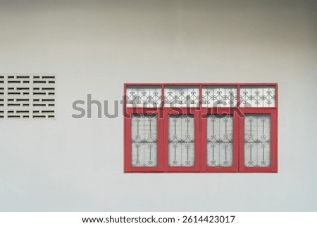 A simple wall featuring a decorative window with red frames and intricate metalwork, complemented by a patterned wall section.