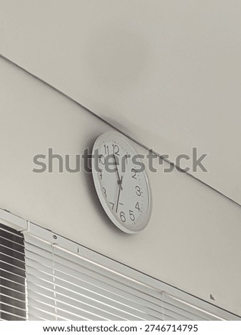 A simple white analog wall clock mounted on a white wall. Modern minimalist timekeeper for office, school, or home interior.