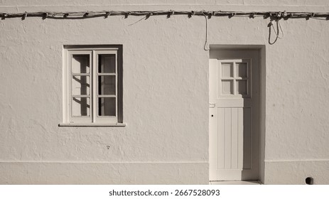 simple whitewashed wall with a small window and wooden door, featuring visible electric cables.