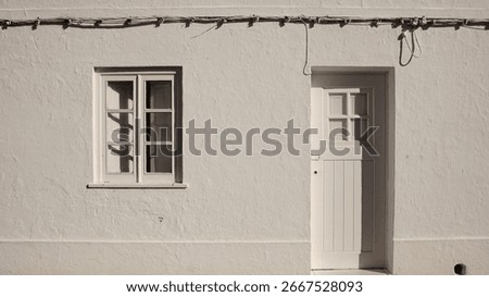 simple whitewashed wall with a small window and wooden door, featuring visible electric cables.