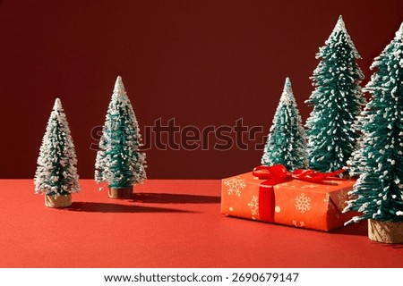 Simple winter forest layout with small pine trees and red surface. Perfect for calm and minimalist Christmas advertisement backgrounds.