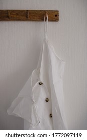 Simple Wooden Wall Hook Hanger With A Hanging Linen White Shirt With Brown Bone Buttons On A White Minimalist Background