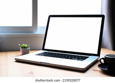 Simple workplace with laptop computer, coffee cup and potted plant on wooden table.