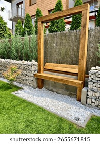 A simple yet inviting scene featuring a wooden bench placed in a contemporary urban garden, surrounded by greenery and modern landscaping. Perfect for themes of relaxation, city life, and urban life.